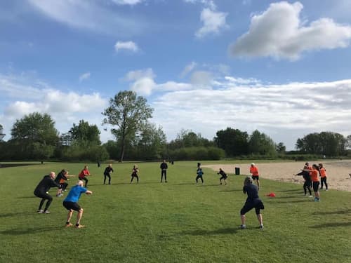 Een groep mensen doen in een cirkel pushups op een met bomen omringd grasveld
